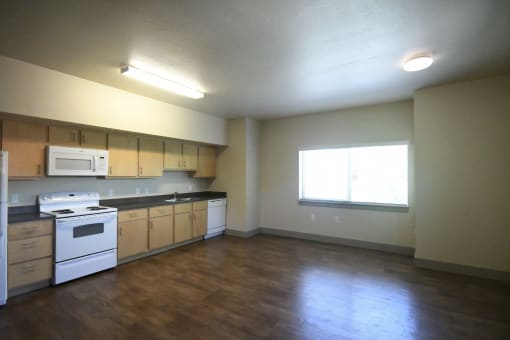 an empty kitchen with white appliances and wooden floors