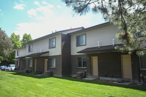 a white and brown apartment building with a lawn and trees