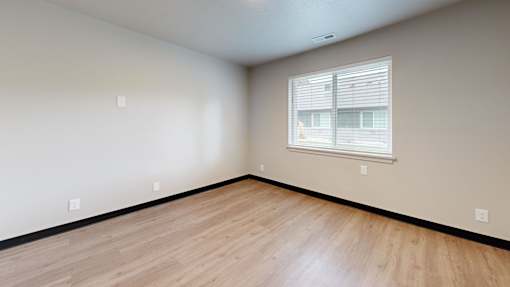 A room with wooden flooring and a window with blinds.