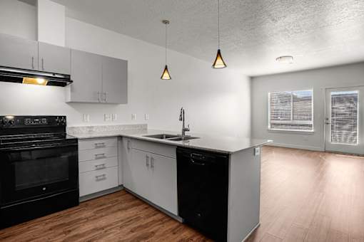 A modern kitchen with black and white appliances and wooden floors.