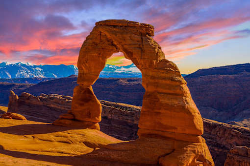 delicate arch with the mountains in the background at sunset