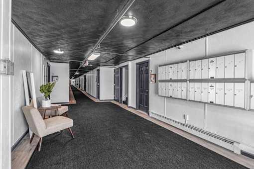 A long hallway with a chair and a plant on the left and lockers on the right.
