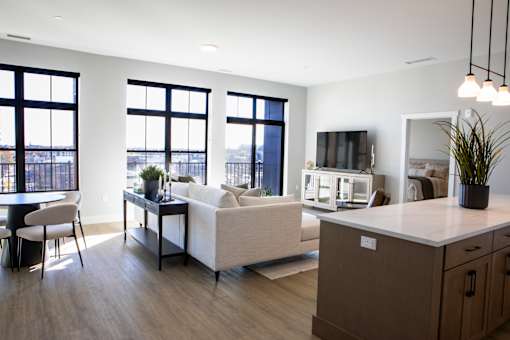 A modern living room with a white couch, a wooden cabinet, and a large window overlooking the city.
