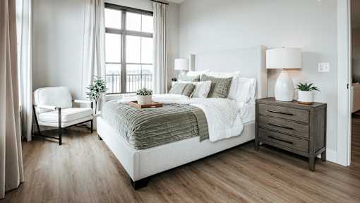 A bedroom with a large bed, a chair, and a nightstand.