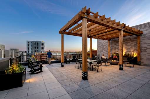 A wooden pergola is situated on a rooftop patio with tables and chairs.