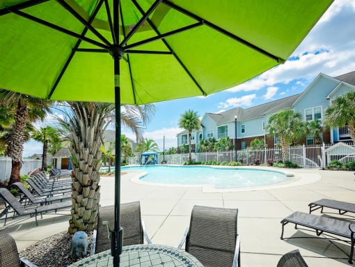 A green umbrella shading chairs by the pool