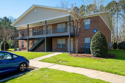 A blue car is parked in front of a two-story brick apartment building.