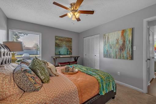 A bedroom with a bed, a ceiling fan, and a painting on the wall.