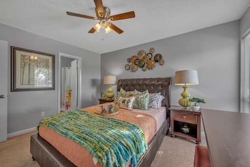 A bedroom with a bed, a ceiling fan, and a wall decoration.