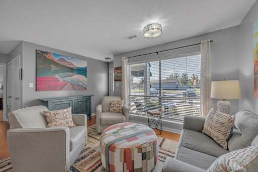 A living room with a large painting on the wall and a view of the outside.