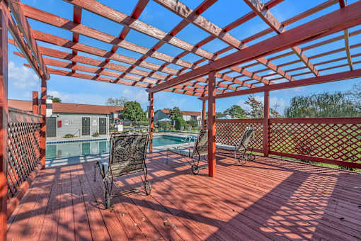 A red wooden pergola with a pool table and chairs underneath it.