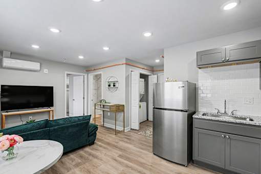 A modern kitchen with a refrigerator, sink, and a living room area with a couch and television at Mayfair Apartments, Kansas City, MO, 64145