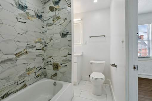 A white toilet sits in a bathroom with a glass mosaic wall at Shipyard Shores Apartments, Newport News