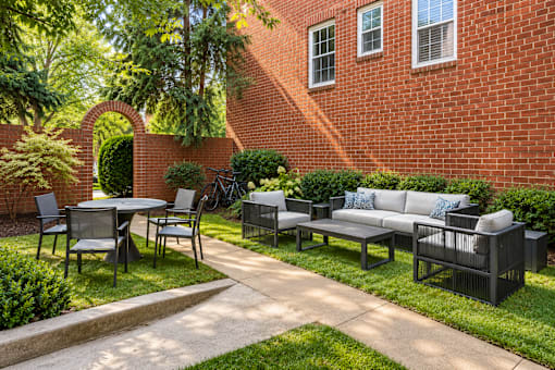A black patio set is on a concrete slab in front of a red brick house.