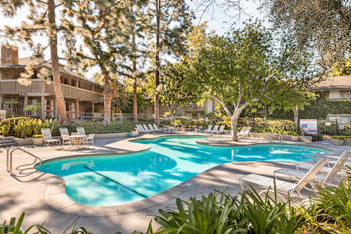 A large outdoor swimming pool surrounded by trees and lounge chairs at The Aspens Riverside, Riverside, 92504