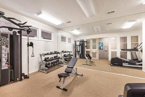 A gym with a variety of equipment including weights, a bench, and a treadmill at The Aspens Riverside, Riverside, 92504