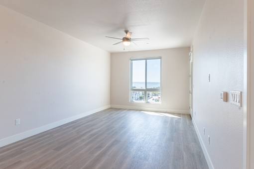 A room with a ceiling fan and a window overlooking a parking lot.