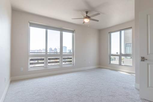 A spacious room with a ceiling fan and large windows overlooking a cityscape.