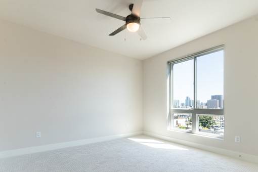 A room with a ceiling fan and a large window overlooking a cityscape.
