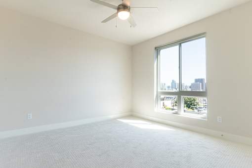 A room with a ceiling fan and a large window overlooking a cityscape.