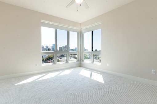 A spacious room with a ceiling fan and large windows overlooking a cityscape.