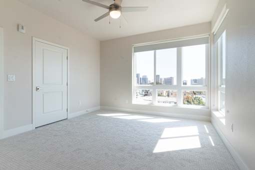 A room with a ceiling fan and large windows overlooking a cityscape.
