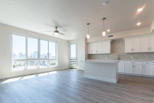 A spacious kitchen and living room with a ceiling fan and large windows.