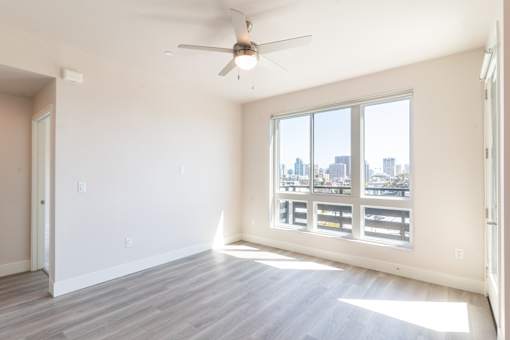 A room with a ceiling fan and a large window overlooking a cityscape.