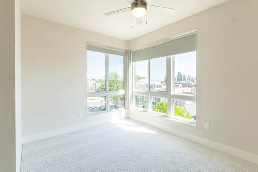 A room with a ceiling fan and large windows overlooking a cityscape.