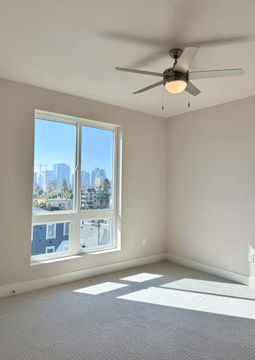 A room with a ceiling fan and a large window overlooking a cityscape.