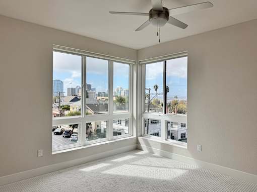 A room with a ceiling fan and large windows overlooking a cityscape.
