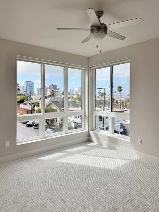 A room with a ceiling fan and large windows overlooking a cityscape.