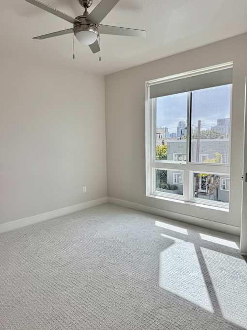 A room with a ceiling fan and a large window showing an outdoor view.