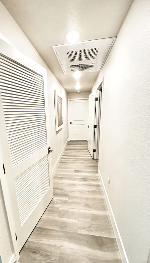 A long, narrow hallway with white walls and a wooden floor.