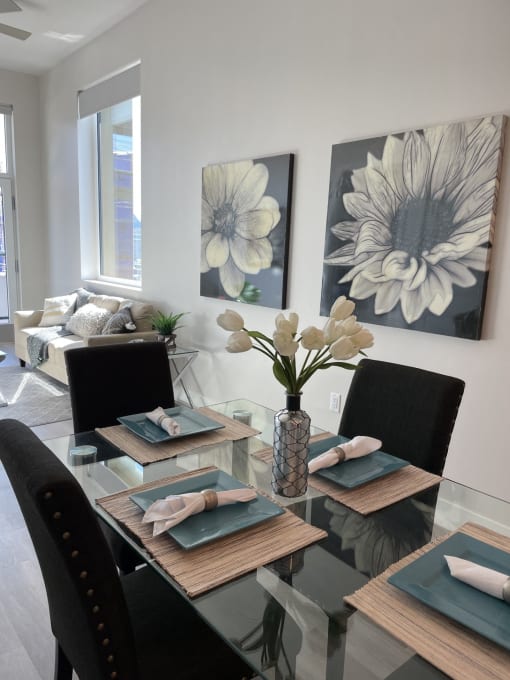 a dining room with a glass table and chairs and paintings on the wall