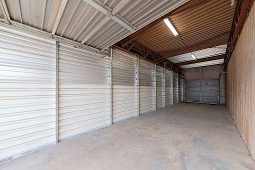 A long, narrow storage unit with a corrugated metal roof and walls, and a row of closed white garage doors.