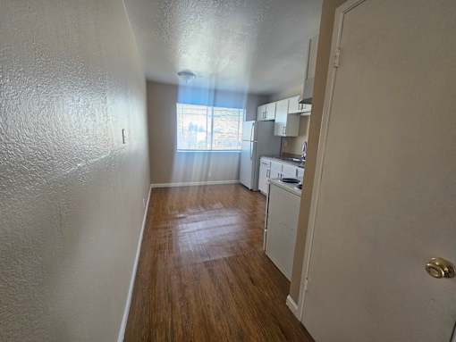 A kitchen area with white cabinets and a wooden floor.