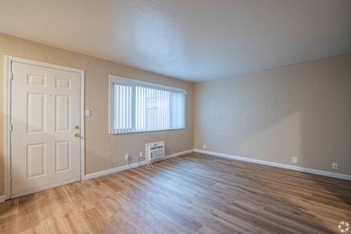 A room with a white door, a window with blinds, and a wooden floor.