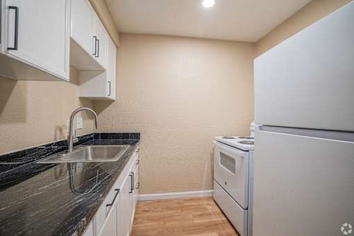 A kitchen with a white refrigerator, sink, and cabinets.