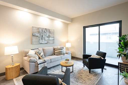 A living room with a grey couch, a black chair, a coffee table, and a large painting on the wall.