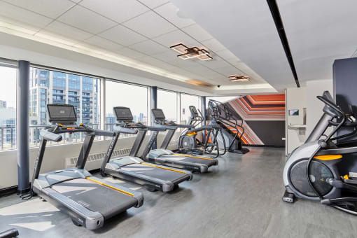 a gym with cardio equipment and a wall of windows