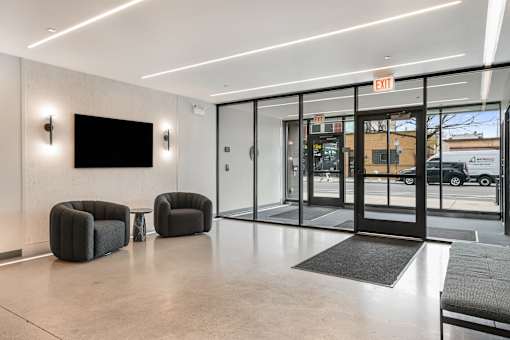 A modern office lobby with a black screen on the wall and two black armchairs.