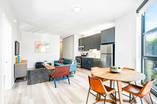 a living room with a table and chairs and a kitchen with stainless steel appliances