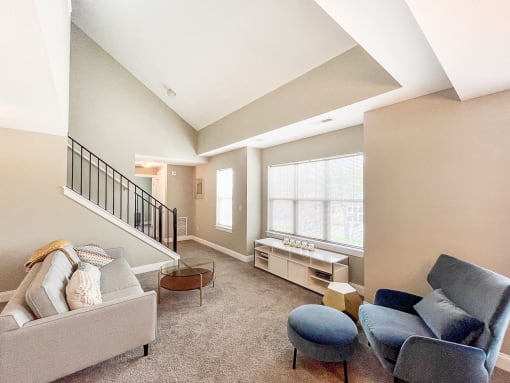Living area of great room with vaulted ceiling, large, bright windows and stairs to second floor loft