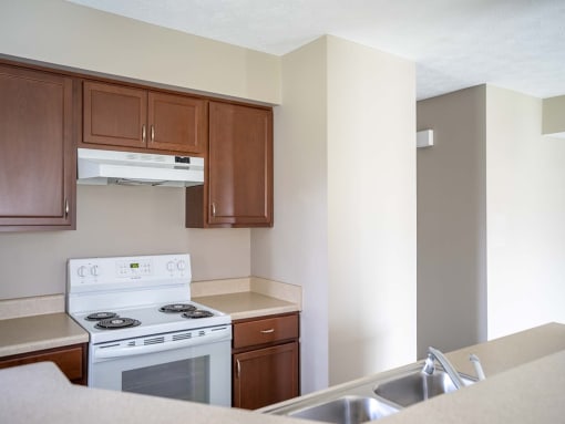 View of kitchen showing electric stove, double kitchen sink, wood cabinetry, and a portion of the breakfast bar