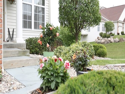the front yard of a white house with flowers in the garden