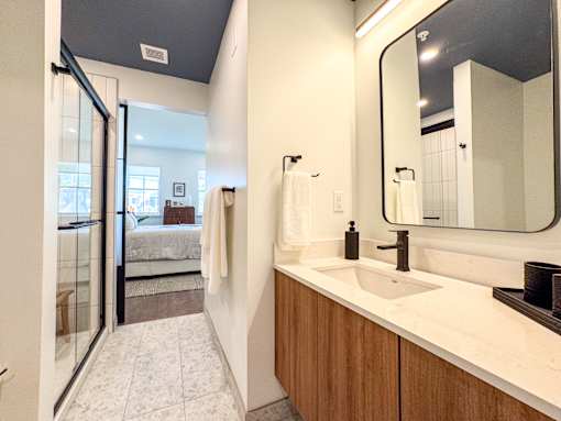 A bathroom with a sink, mirror, and a glass door leading to a bedroom.