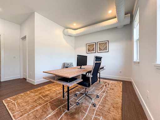 A room with a brown rug and a wooden table with two chairs.
