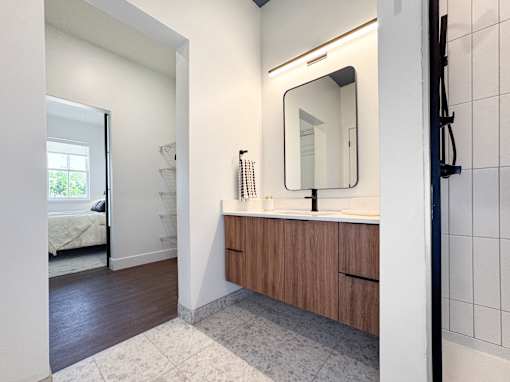 A bathroom with a mirror, sink, and a bedroom in the background.