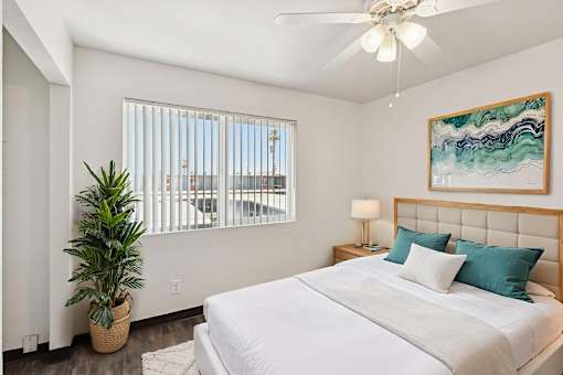A bedroom with a large bed, a ceiling fan, and a plant.